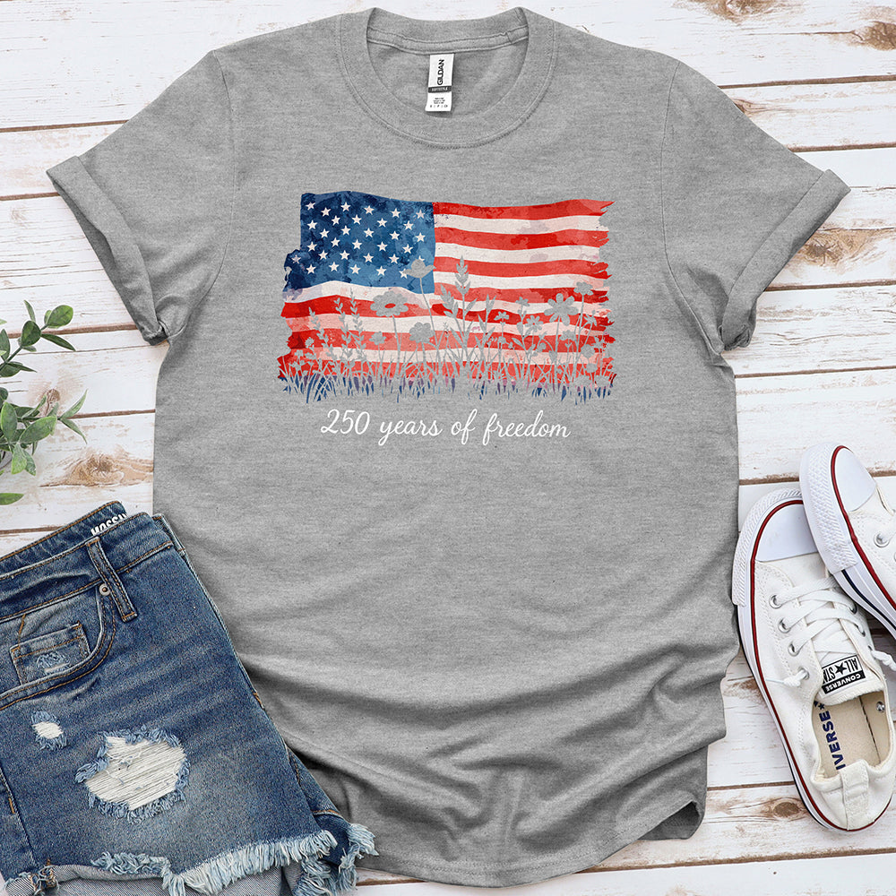 Sport grey t-shirt with American flag and '250 years of freedom' text, laid flat with denim shorts and white sneakers.