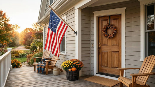 American flag displayed on a clean front porch beside a wooden door and autumn flowers