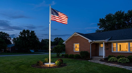 American flag flying from a tall illuminated flagpole beside a brick home at dusk
