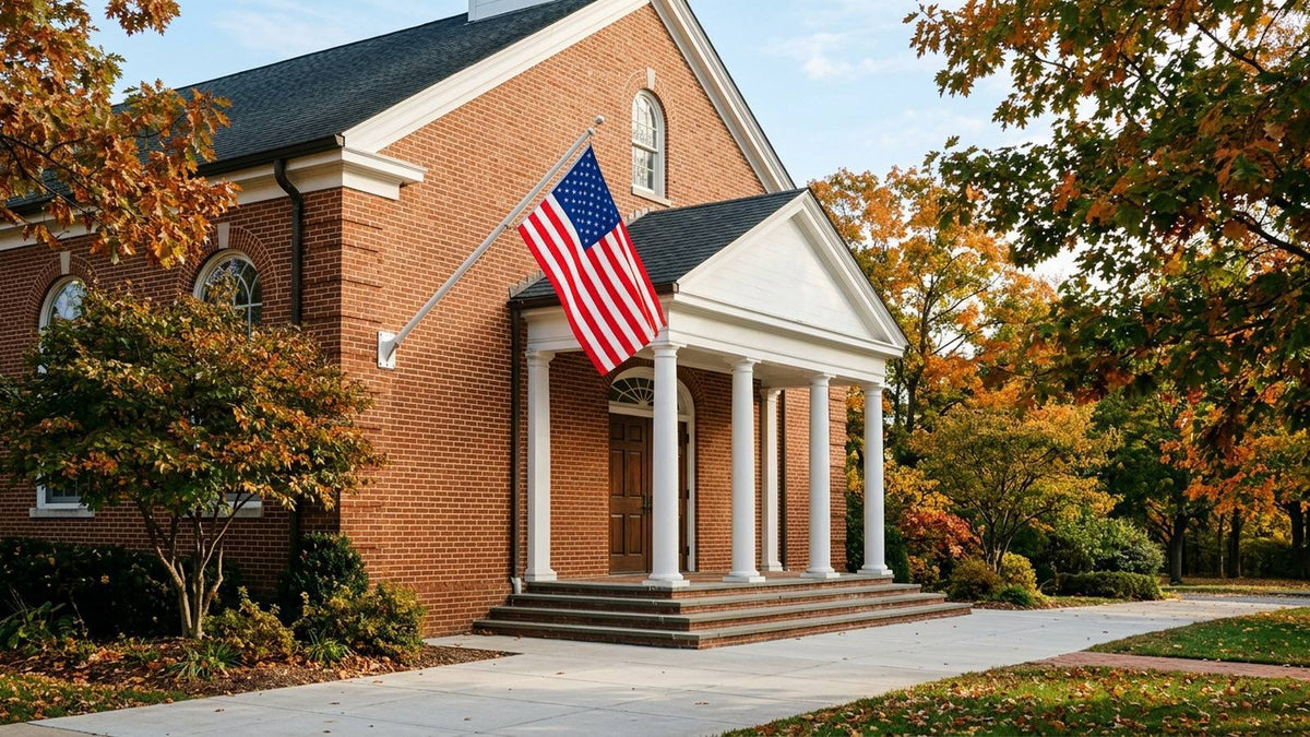 American flag displayed on a wall bracket outside a brick church in autumn