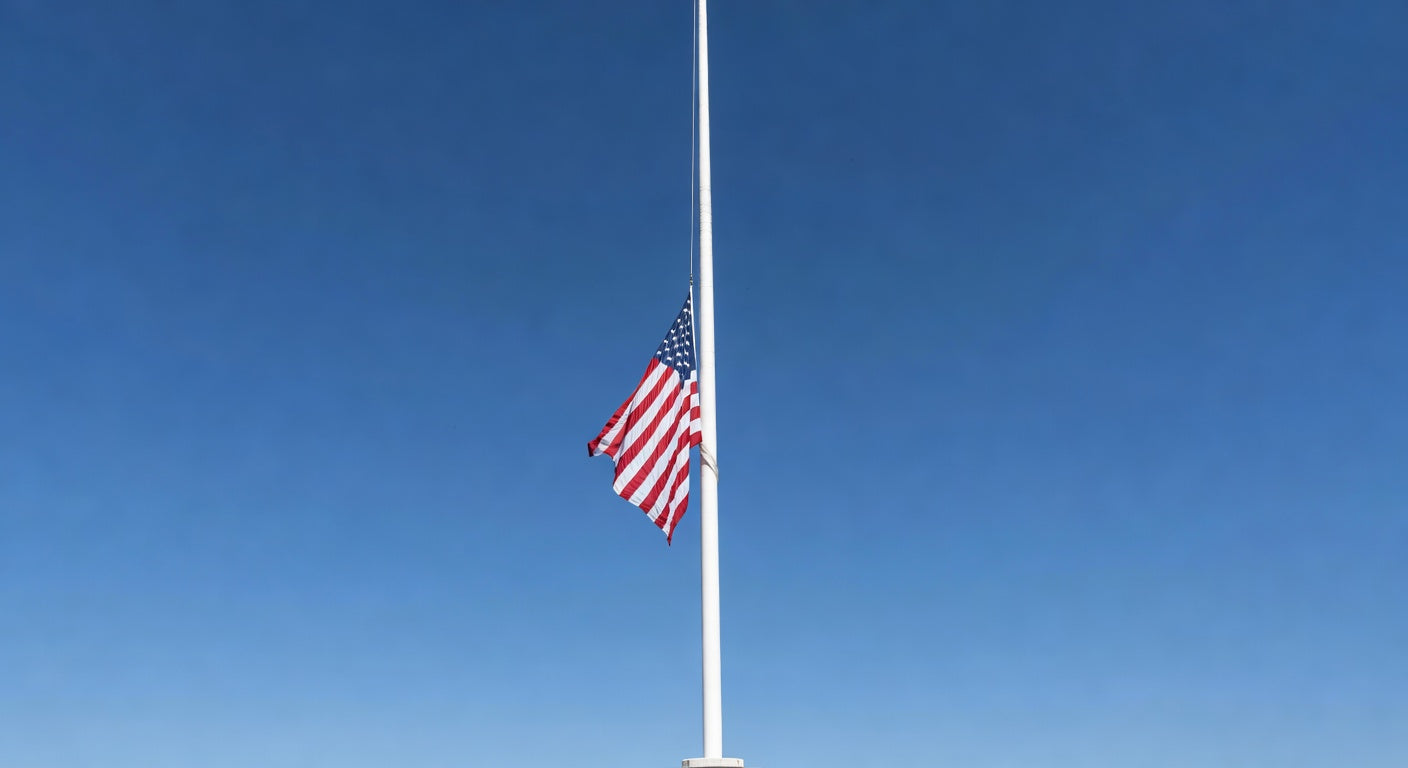 American flag at half-staff on flagpole against clear blue sky