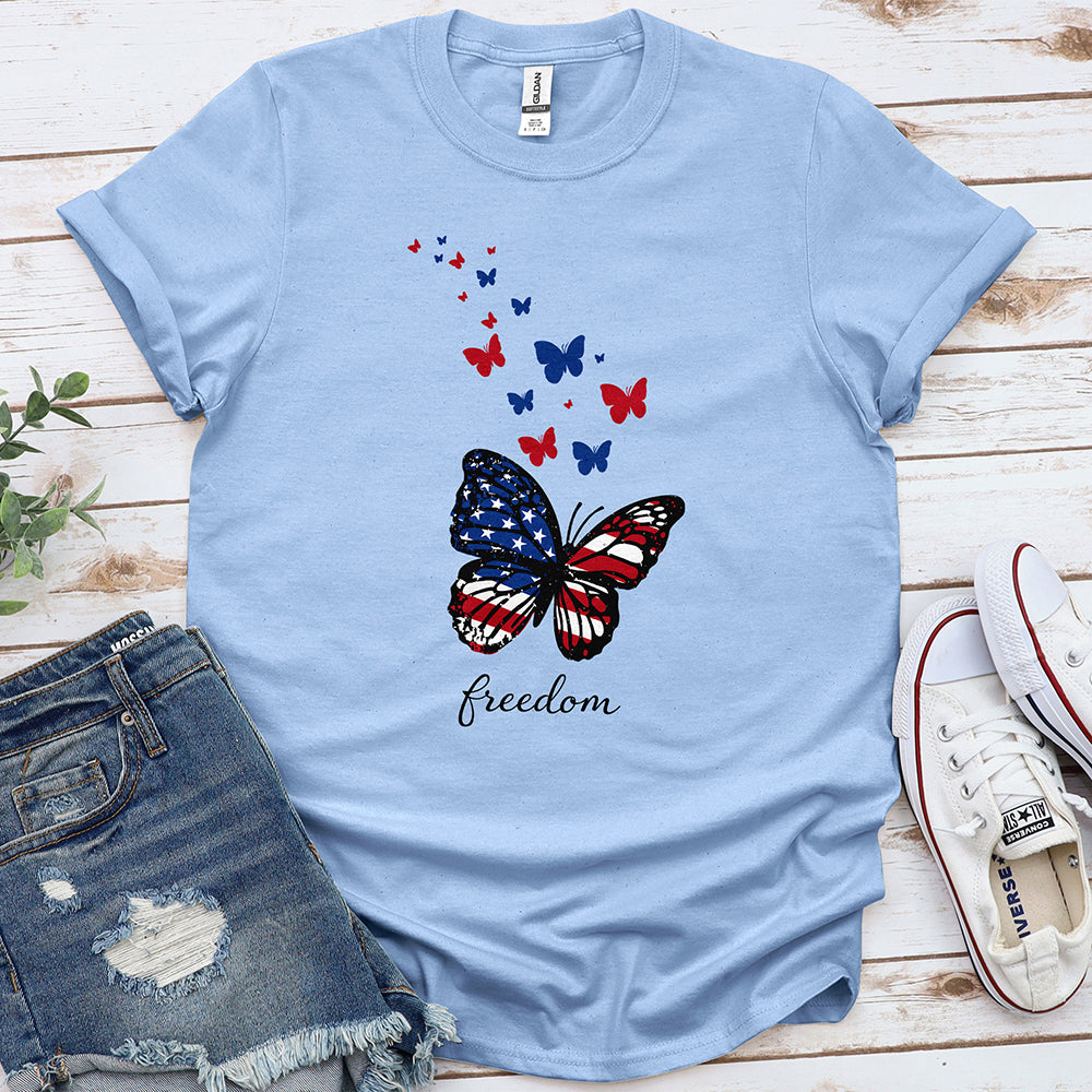 Light blue t-shirt with butterfly in American flag colors and 'freedom' text, laid flat with denim shorts and white sneakers.