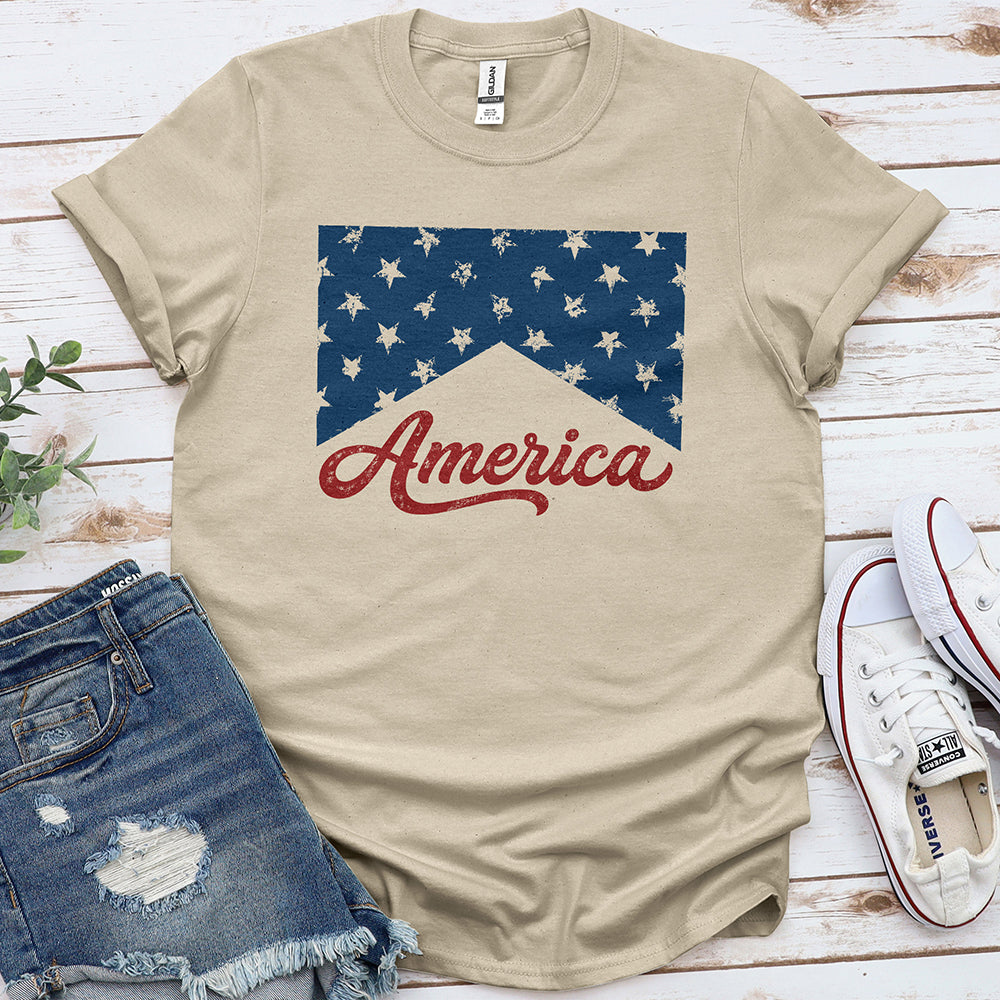 Sand-colored t-shirt with distressed stars and 'America' text, styled with denim shorts