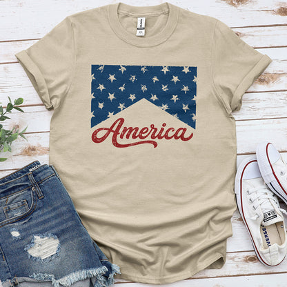 Sand-colored t-shirt with distressed stars and 'America' text, styled with denim shorts