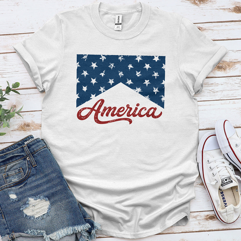 White patriotic t-shirt with blue stars and red 'America' text, styled with denim shorts and sneakers