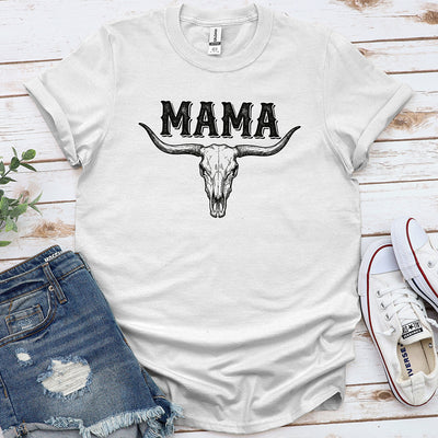 White graphic tee with 'MAMA' and a bull skull design, styled with denim shorts and sneakers