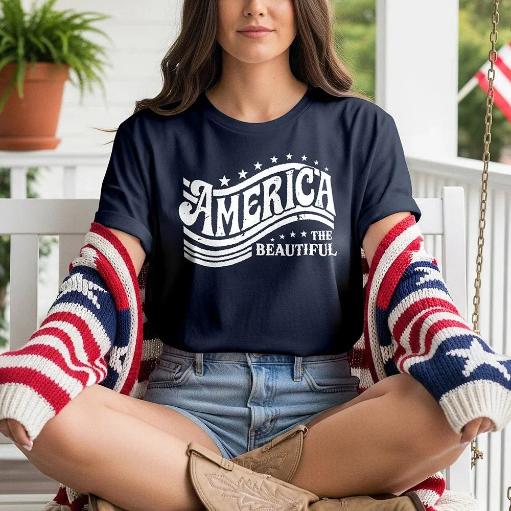 Woman wearing 'America the Beautiful' navy tee, patriotic cardigan, denim shorts on porch