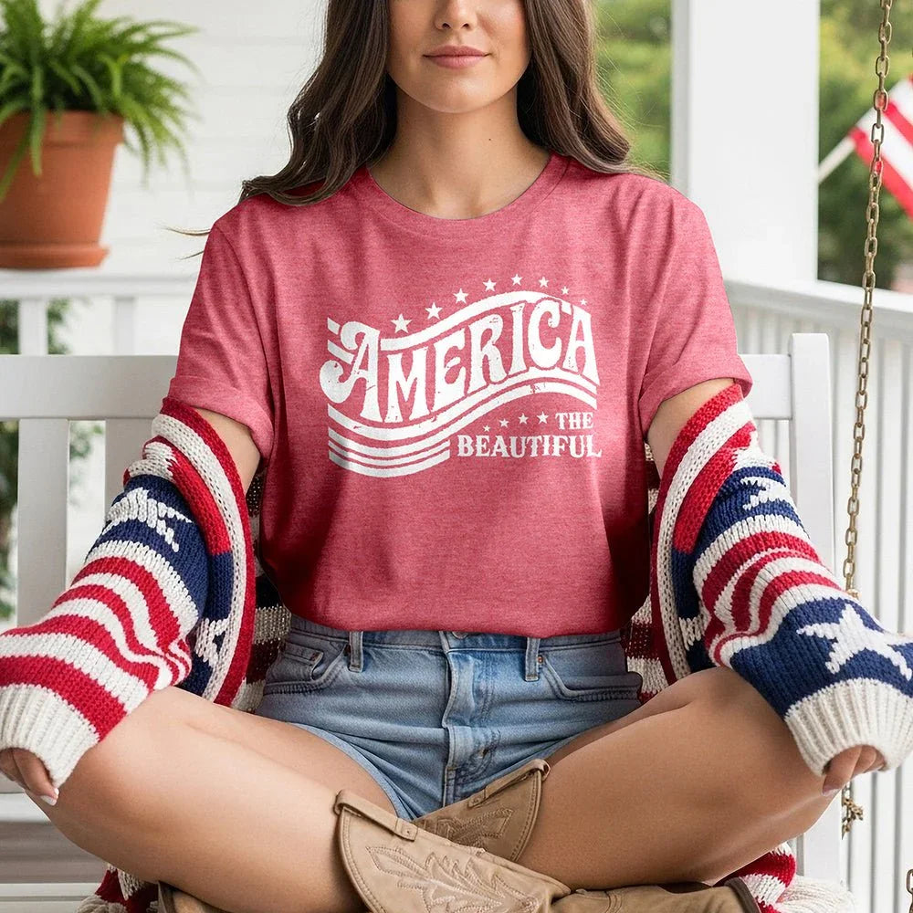 Woman wearing America the Beautiful graphic tee, patriotic cardigan, and denim shorts on porch