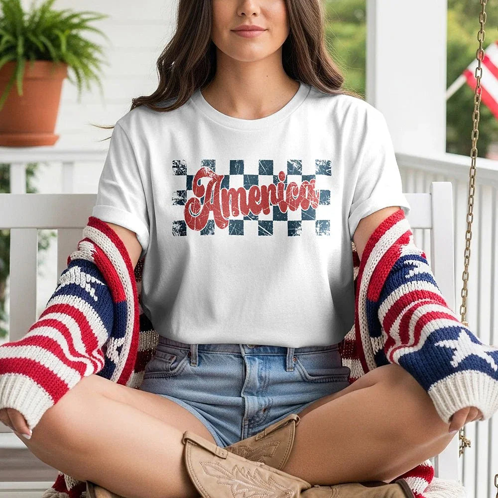 Woman on porch wearing American checkerboard tee, denim shorts, and patriotic sweater.