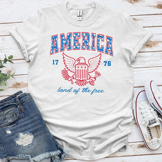 White t-shirt with American eagle crest, 'America 1776' text, and 'land of the free' slogan.