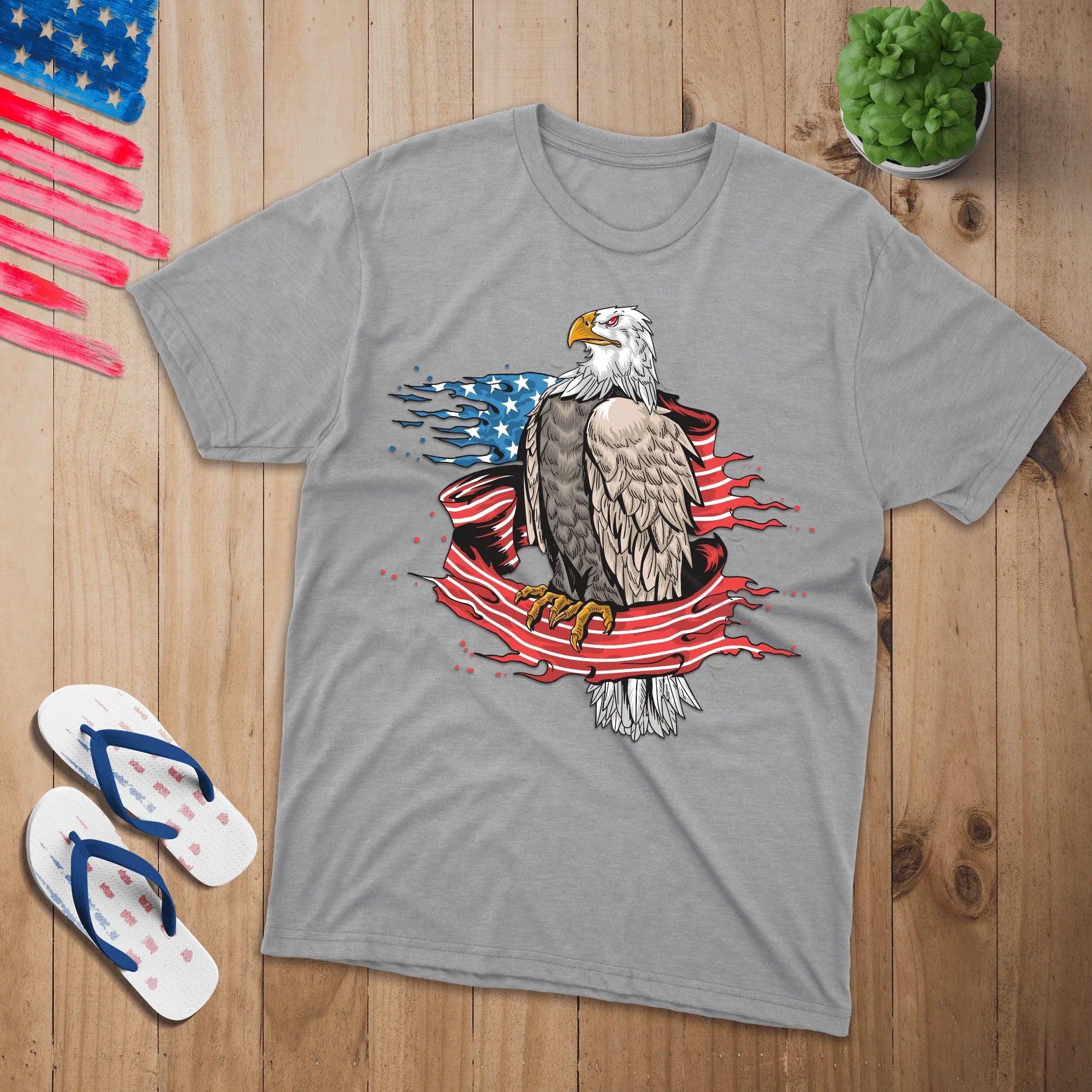 Gray t-shirt with bald eagle and American flag graphic, flat lay with sandals and plant