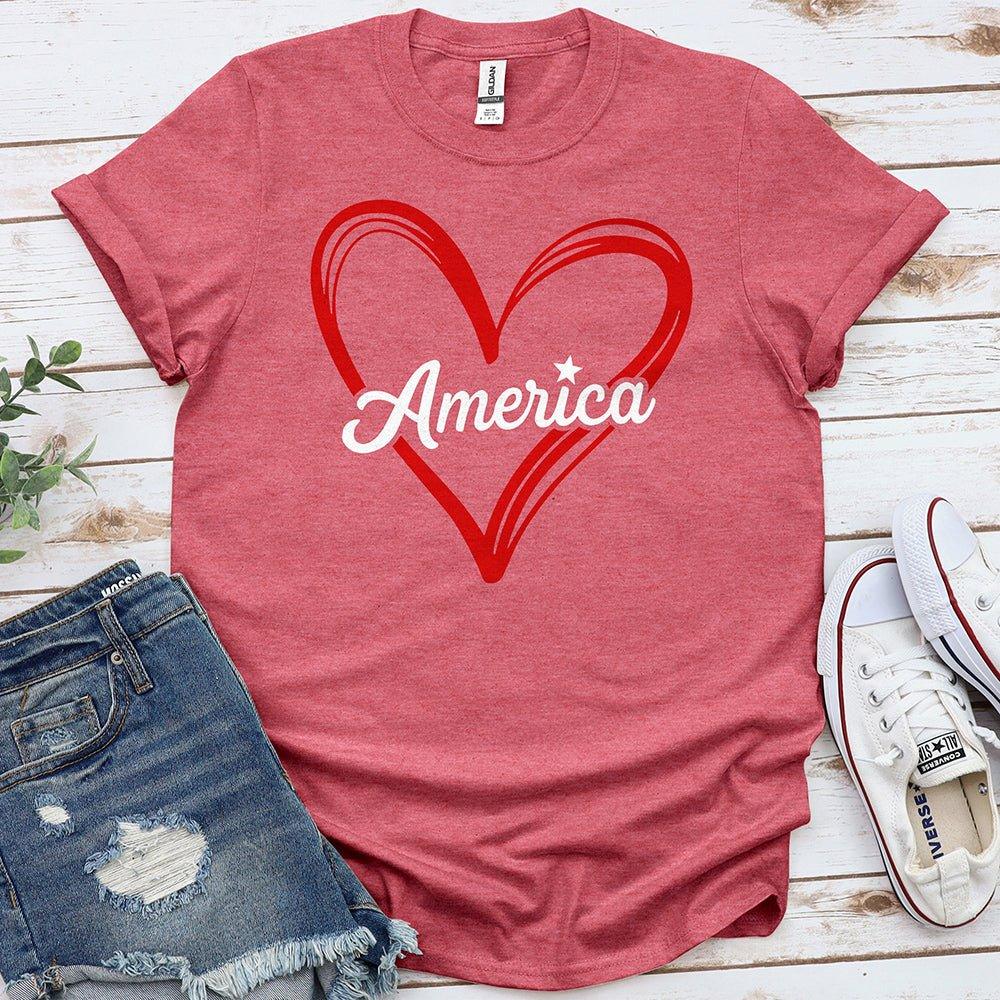 Red America heart graphic t-shirt with denim shorts and white sneakers on wood background