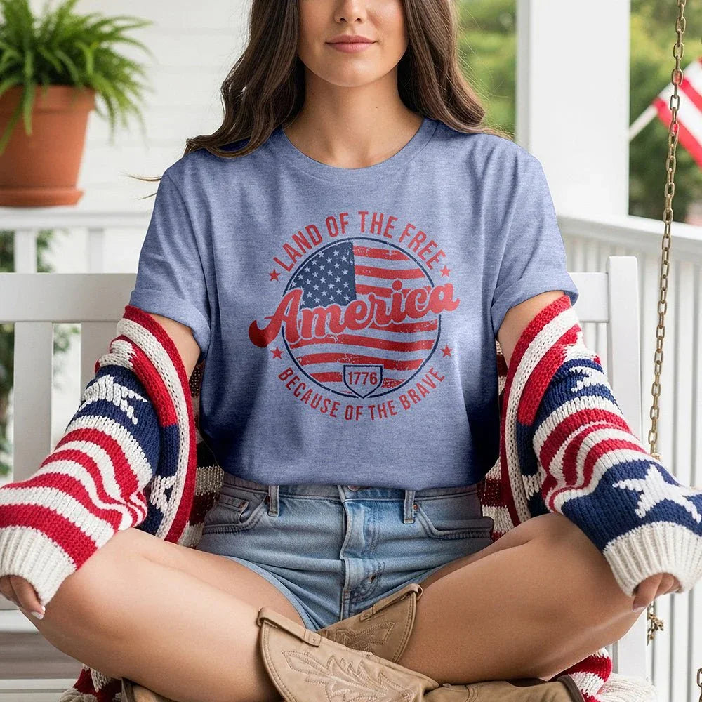 Woman wearing 'Land of the Free America Because of the Brave' tee with USA flag sweater on porch