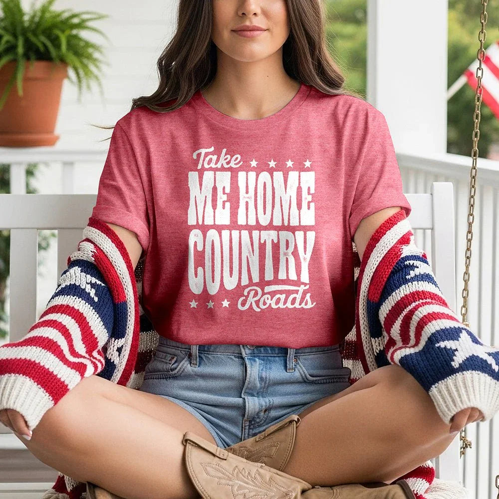 Woman in red 'Take Me Home Country Roads' tee, denim shorts, patriotic cardigan, and cowboy boots on a porch