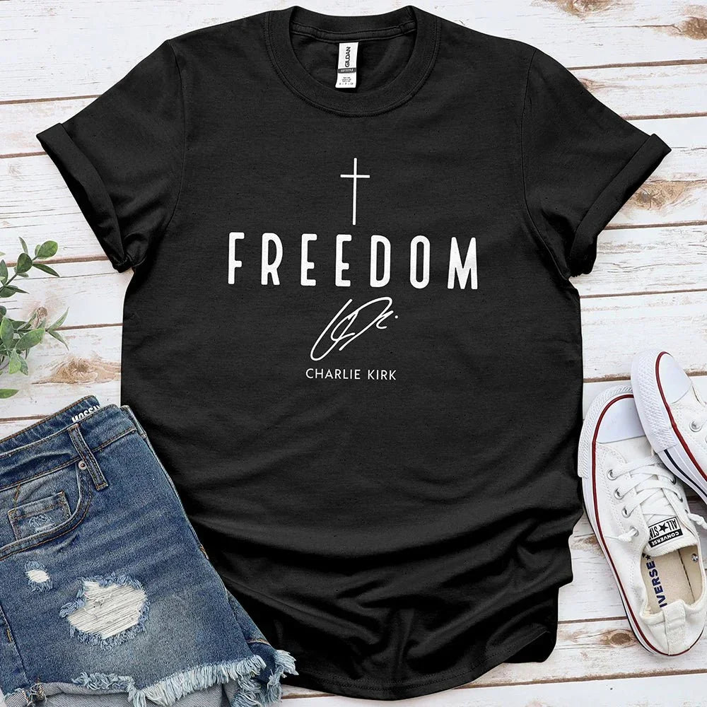 Black Freedom tee with cross graphic laid on wood, paired with ripped denim shorts and white sneakers
