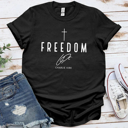Black Freedom tee with cross graphic laid on wood, paired with ripped denim shorts and white sneakers