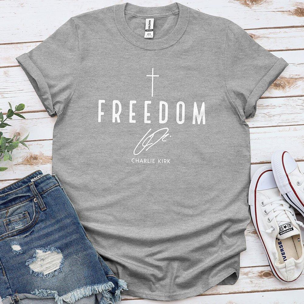 Gray Freedom tee with cross and signature, styled with denim shorts and white sneakers on wood