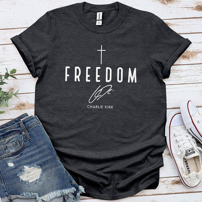 Freedom graphic tee with cross, denim shorts, and sneakers on wood background