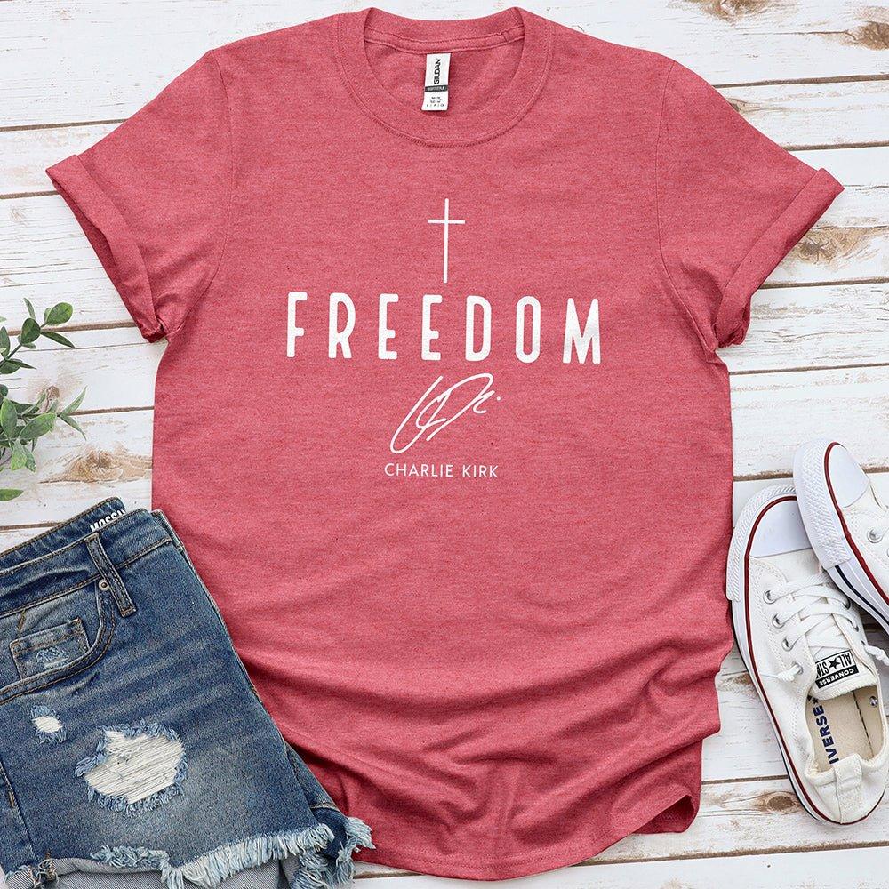 Red Freedom t-shirt with cross and text, styled with denim shorts and white sneakers on wood