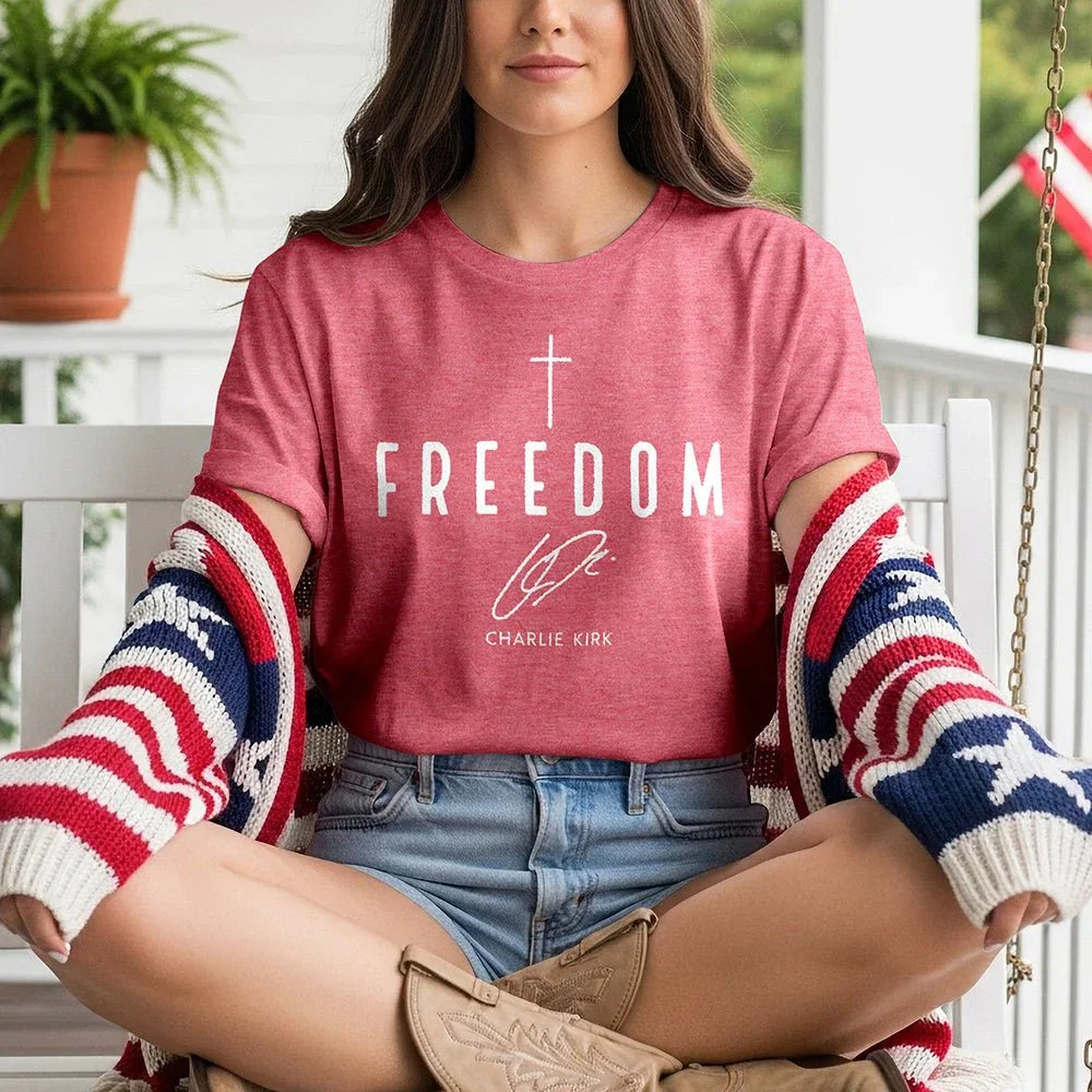 Woman on porch wearing red Freedom tee, patriotic sweater, denim shorts, and cowboy boots.