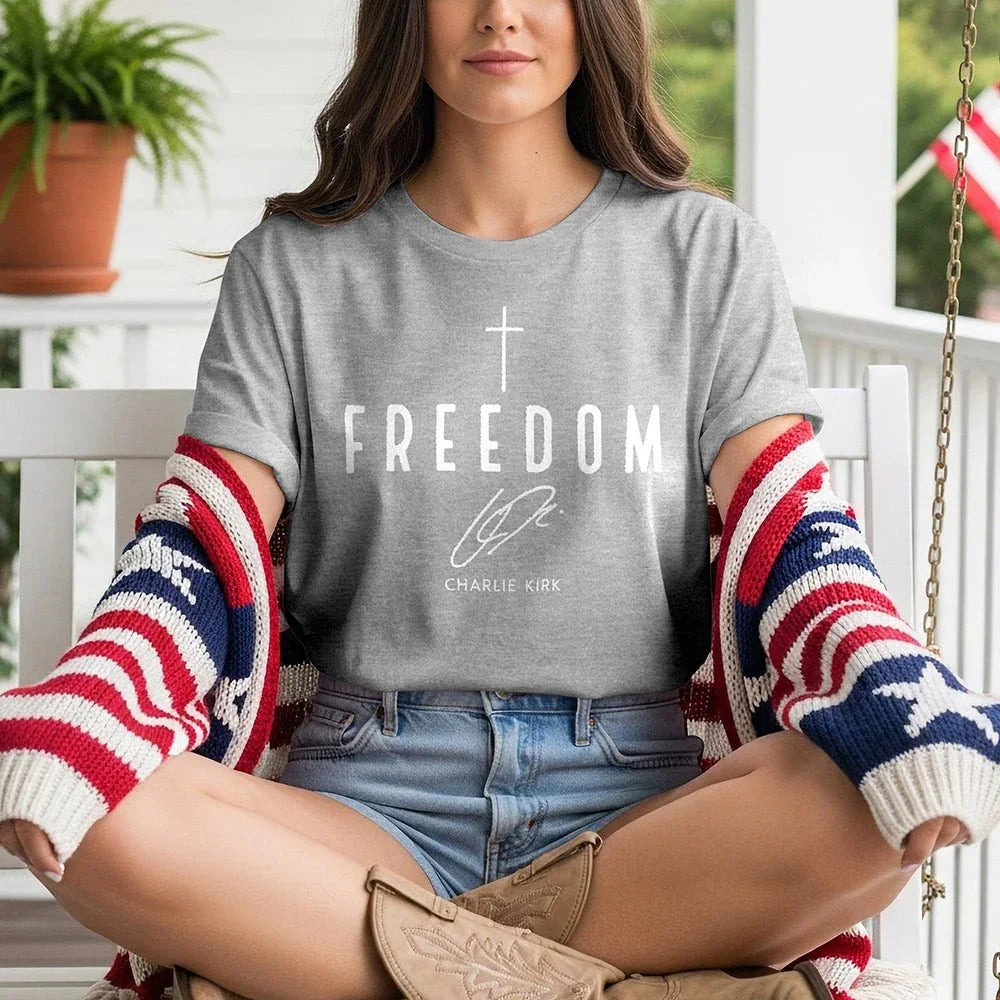 Woman on porch in Proud & Free Freedom tee, patriotic sweater, denim shorts, and cowboy boots