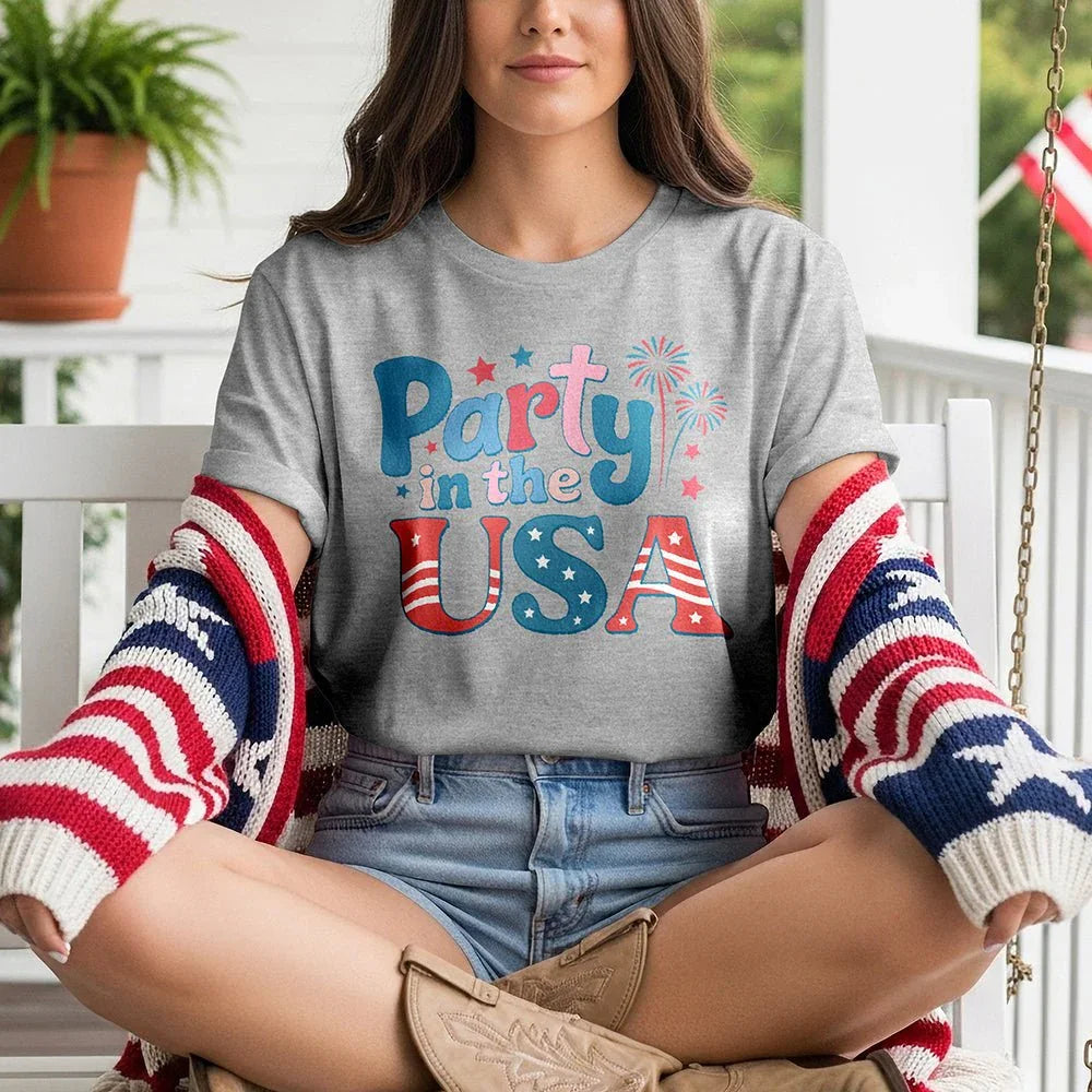 Woman wearing 'Party in the USA' t-shirt and patriotic sweater on porch, Proud & Free style