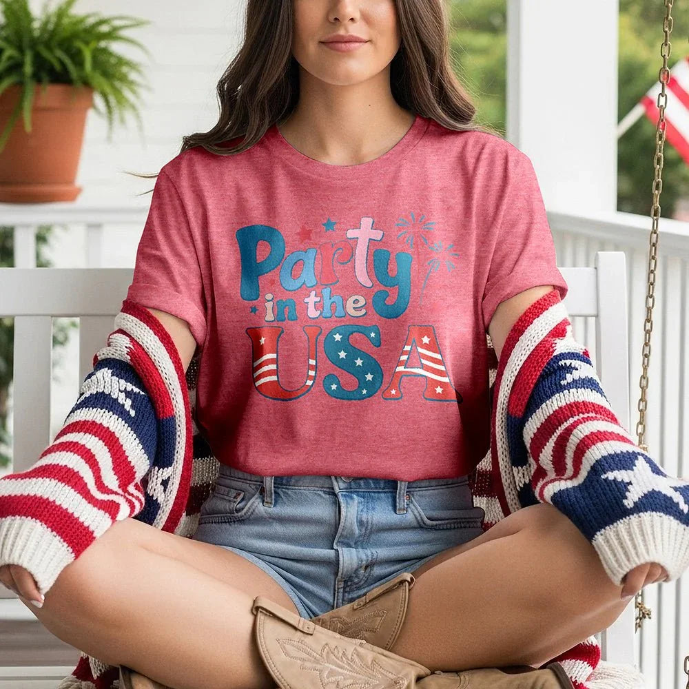 Woman on porch in red 'Party in the USA' tee, denim shorts, patriotic cardigan, cowboy boots