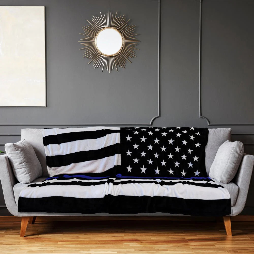 Thin blue line plush blanket with American flag design draped on a grey sofa in modern living room