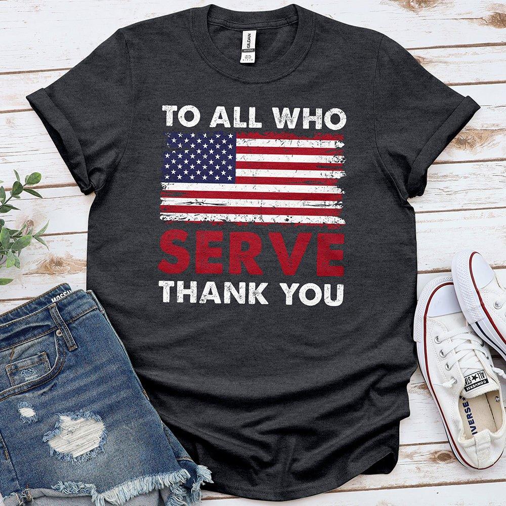 Black T-shirt with distressed American flag and 'To All Who Serve Thank You' message, laid out with denim shorts and white sneakers on a wooden surface.