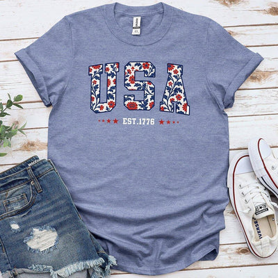 Blue floral USA t-shirt with 'EST. 1776' text, styled with denim shorts and white sneakers